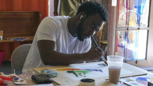A black man in a white shirt paints with a brush.