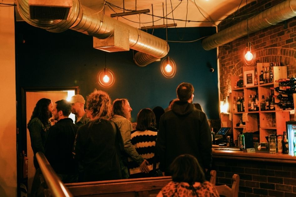 Several people are standing in a queue at the bar at The Tin Music and Arts.